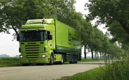 HD desktop wallpaper featuring a bright green Scania truck driving on a tree-lined road under a clear sky.