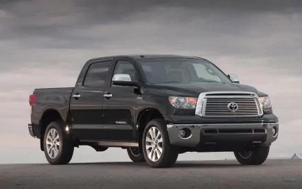 HD PC desktop wallpaper featuring a black Toyota off-road vehicle parked on a flat, open surface under a cloudy sky.