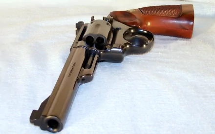 High-definition desktop wallpaper featuring a Smith & Wesson revolver handgun with a wooden grip, displayed on a soft, light surface.