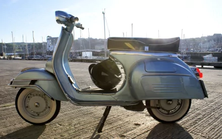 A sleek blue scooter parked on a textured pavement, with a marina and boats in the background on a sunny day. This HD image serves as a vibrant desktop wallpaper and background.