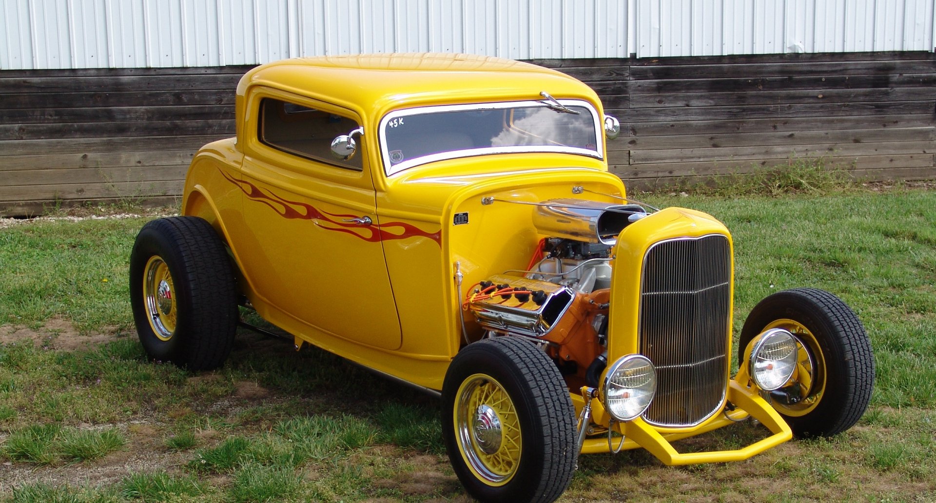 A vibrant yellow hot rod car with flame decals and exposed engine, captured outdoors on grass; a high-definition PC desktop wallpaper and background.