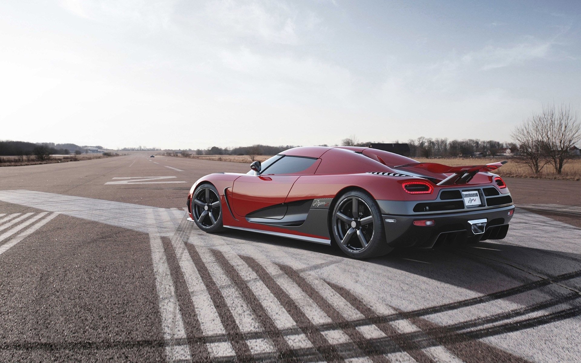 HD PC desktop wallpaper featuring a red Koenigsegg sports car on an open road with clear skies and tire marks on the pavement.