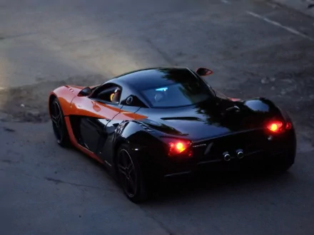 HD PC desktop wallpaper and background: rear three-quarter view of a black-and-orange Marussia sports car on asphalt at dusk, taillights glowing.