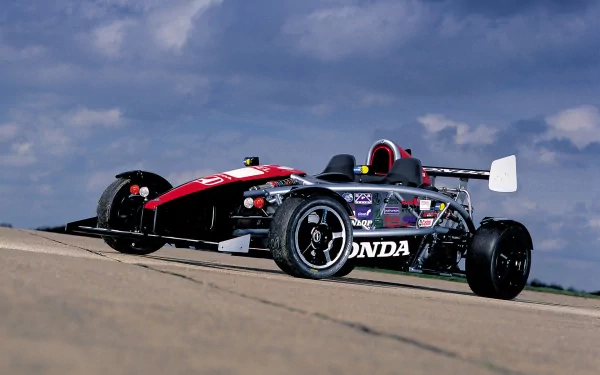 HD PC desktop wallpaper background: red and black Ariel Atom vehicle racing on a track beneath a dramatic cloudy sky.