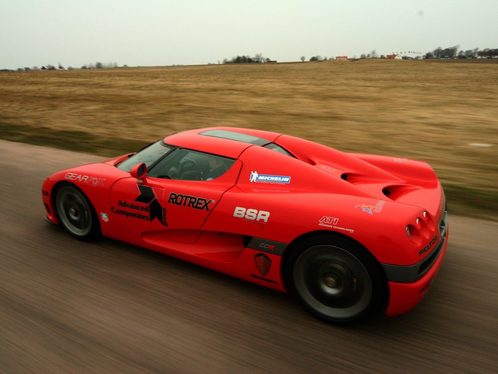 Red Koenigsegg vehicle racing along a country road; dynamic HD PC desktop wallpaper/background with motion blur and open landscape.
