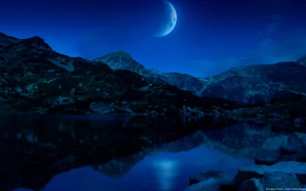 HD desktop wallpaper featuring a crescent moon glowing over a mountain landscape with a tranquil lake reflecting the night sky in a fantasy-inspired scenic photograph.