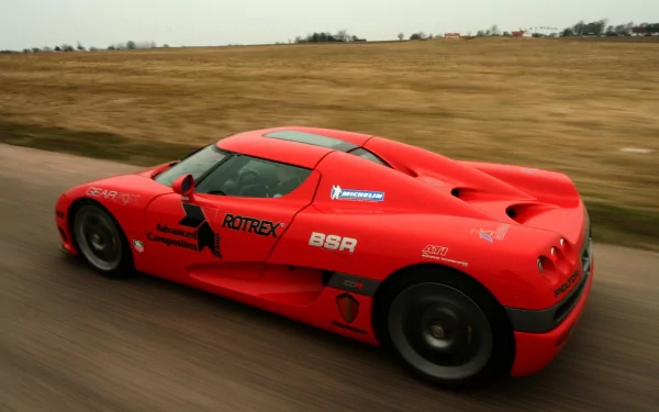 Red Koenigsegg vehicle racing along a country road; dynamic HD PC desktop wallpaper/background with motion blur and open landscape.