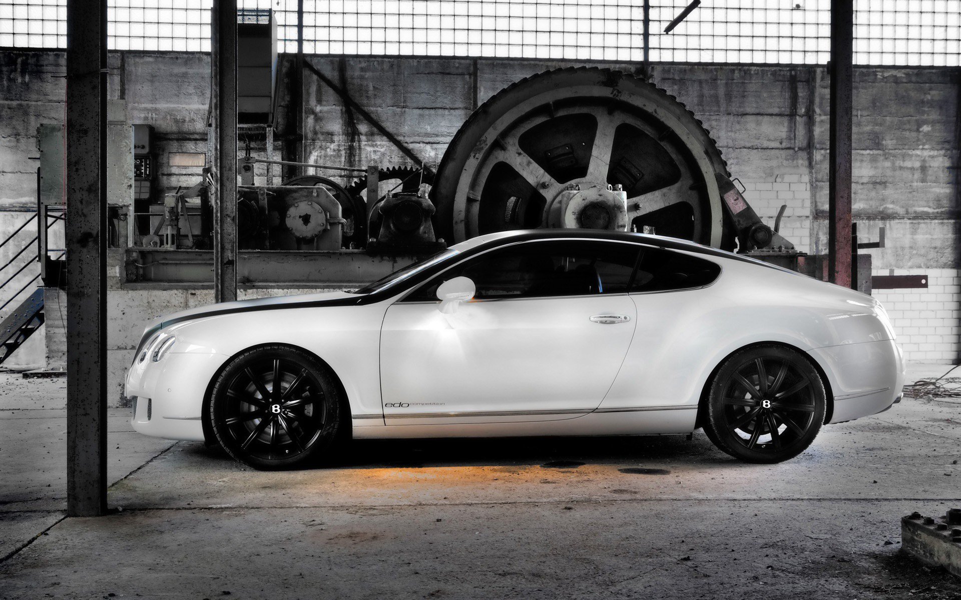 HD PC desktop wallpaper featuring a sleek white Bentley parked inside an industrial garage with large machinery in the background.