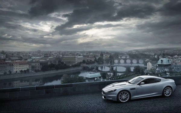 A stunning Aston Martin DBS parked on a scenic overlook, with a dramatic cloudy sky and a cityscape in the background, creating an elegant and captivating desktop wallpaper.