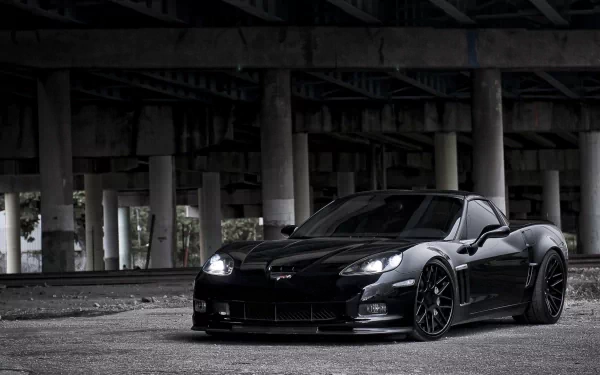 HD PC desktop wallpaper/background of a black Chevrolet Corvette vehicle parked beneath a concrete overpass, low-angle view with dramatic lighting and reflective surfaces.