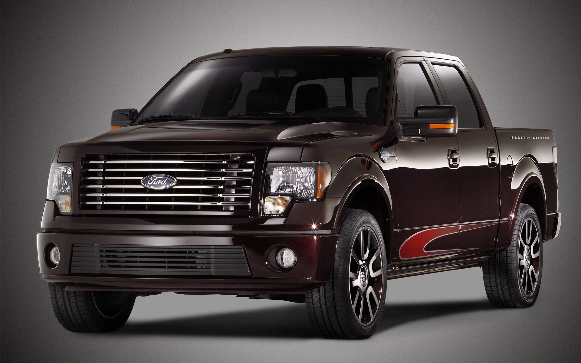 HD PC desktop wallpaper of a Ford F-150 vehicle: dark maroon crew-cab pickup in three-quarter front view with chrome grille and red side decal on a gray background.