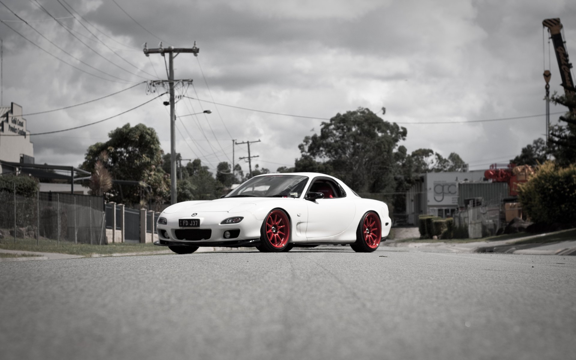 HD PC desktop wallpaper background: white Mazda sports car with red rims parked on an industrial street under a cloudy sky.