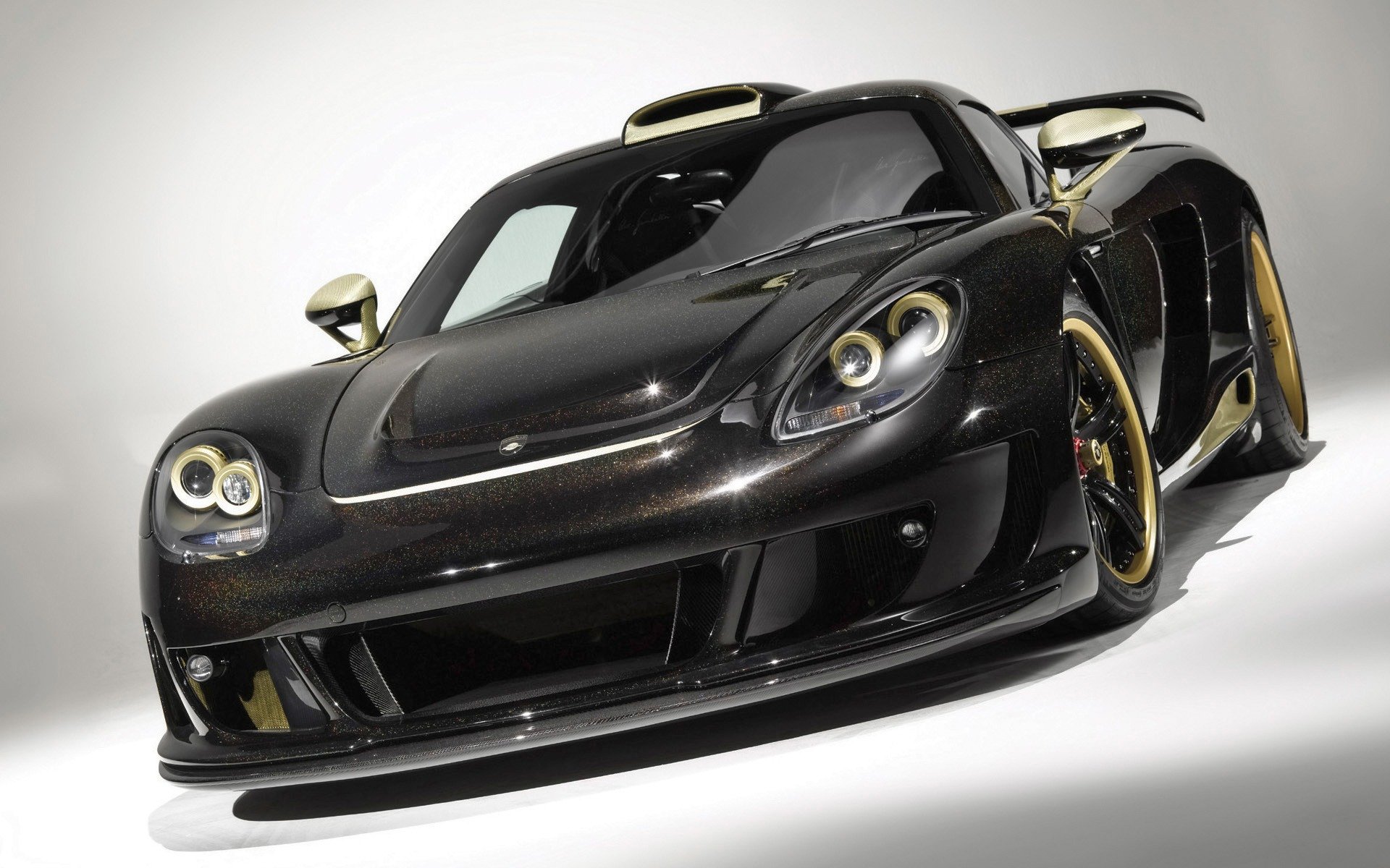 Low-angle studio shot of a sleek black Porsche vehicle — a sports car with gold-accent wheels, glossy bodywork and aggressive aero; HD PC desktop wallpaper/background.