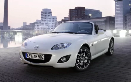 White Mazda convertible on a waterfront boardwalk with city skyline at dusk — HD PC desktop wallpaper and background.