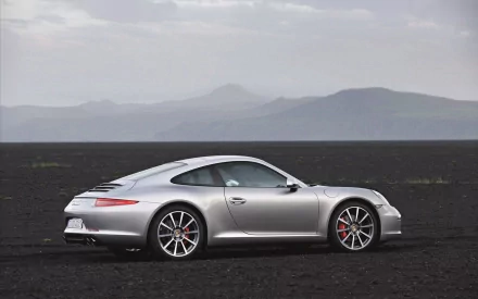 Silver Porsche sports coupe on a black volcanic plain with distant mountains — HD PC desktop wallpaper and background.