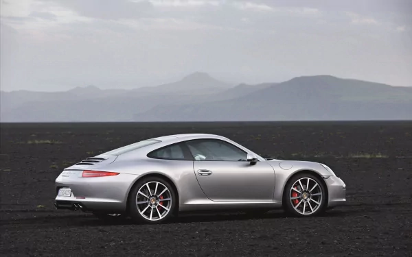 Silver Porsche sports coupe on a black volcanic plain with distant mountains — HD PC desktop wallpaper and background.