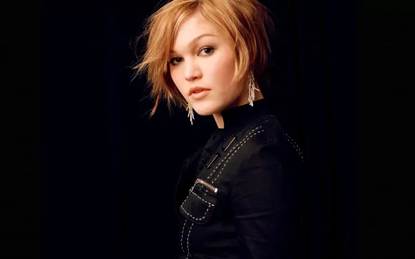 A high-definition desktop wallpaper featuring celebrity Julia Stiles with short blonde hair, wearing a black outfit and earrings, set against a dark background.