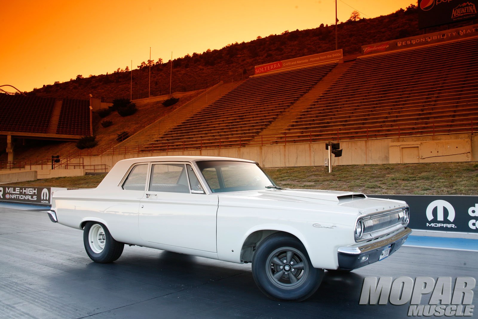 HD PC desktop wallpaper featuring a classic white Dodge vehicle parked on a racetrack at sunset with empty stands in the background.