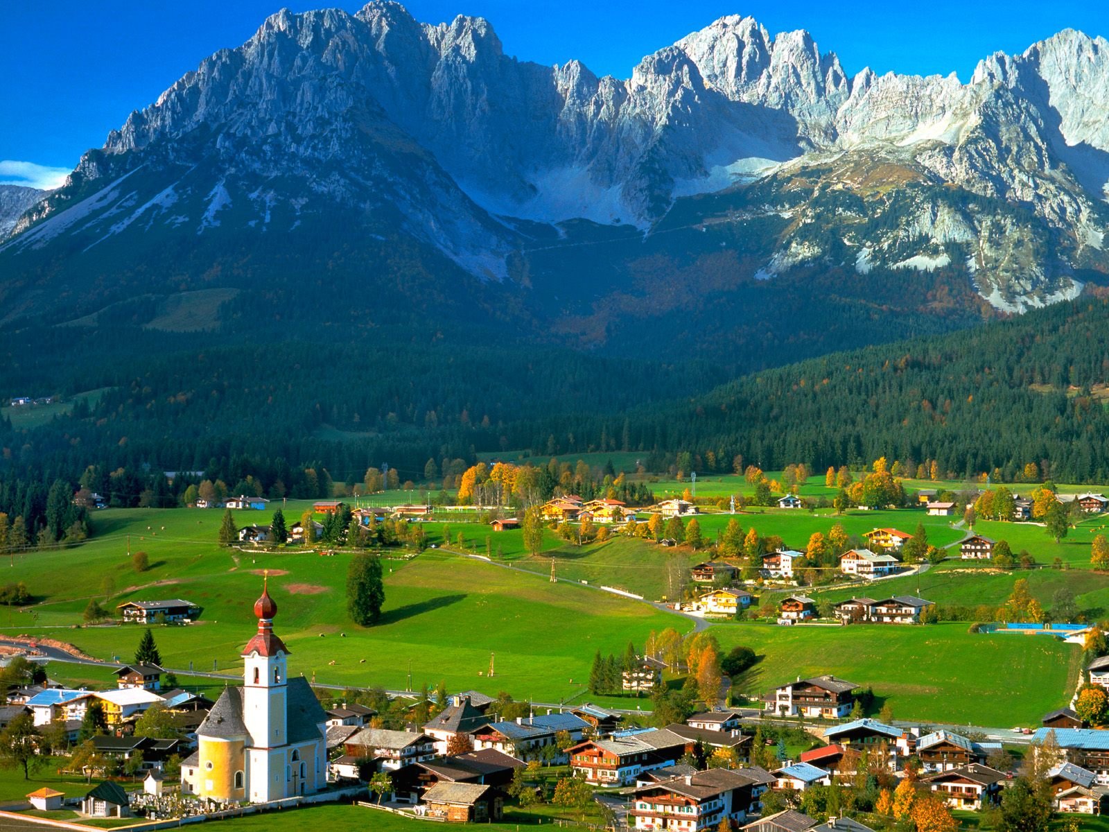 Photography landscape: HD PC desktop wallpaper background of a green Alpine valley village with church steeple beneath towering snow-capped mountains.