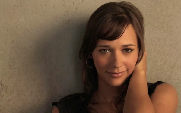 A striking HD wallpaper featuring celebrity Rashida Jones, showcasing her warm smile and casual pose against a textured background.