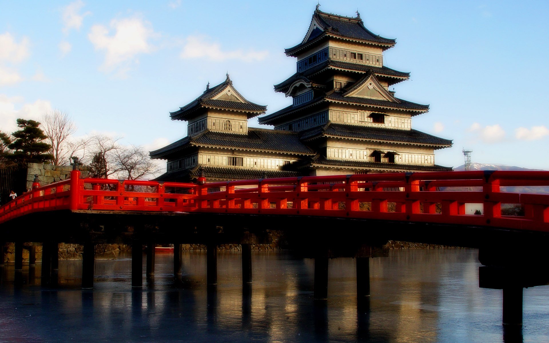 A stunning HD desktop wallpaper featuring a majestic castle with traditional architecture, set against a bright sky and complemented by a vibrant red bridge in the foreground.