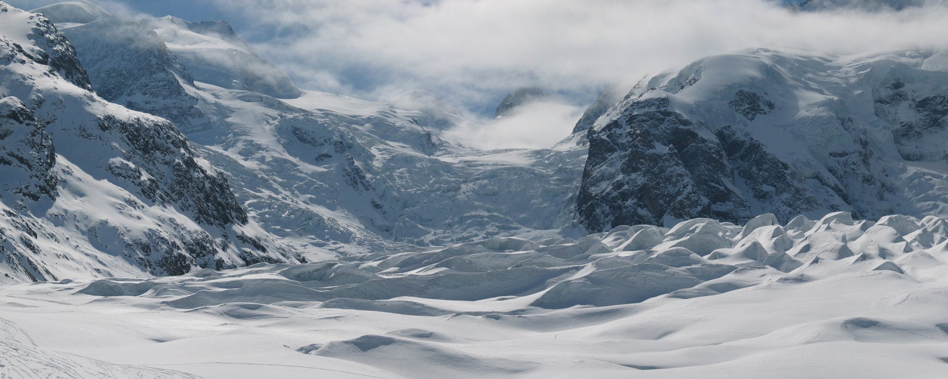 HD PC desktop wallpaper and background: expansive winter nature landscape of wind-sculpted snow and rugged mountain peaks under a brooding sky.