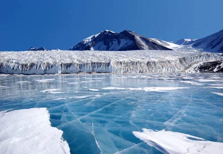 HD wallpaper of an Arctic winter scene, showcasing a frozen ice landscape with towering mountains under a clear blue sky.