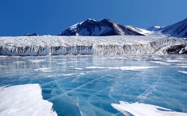 HD wallpaper of an Arctic winter scene, showcasing a frozen ice landscape with towering mountains under a clear blue sky.