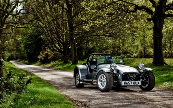 Caterham sports car on a tree-lined country road, vivid greens and sunlight — HD PC desktop wallpaper/background with crisp detail.