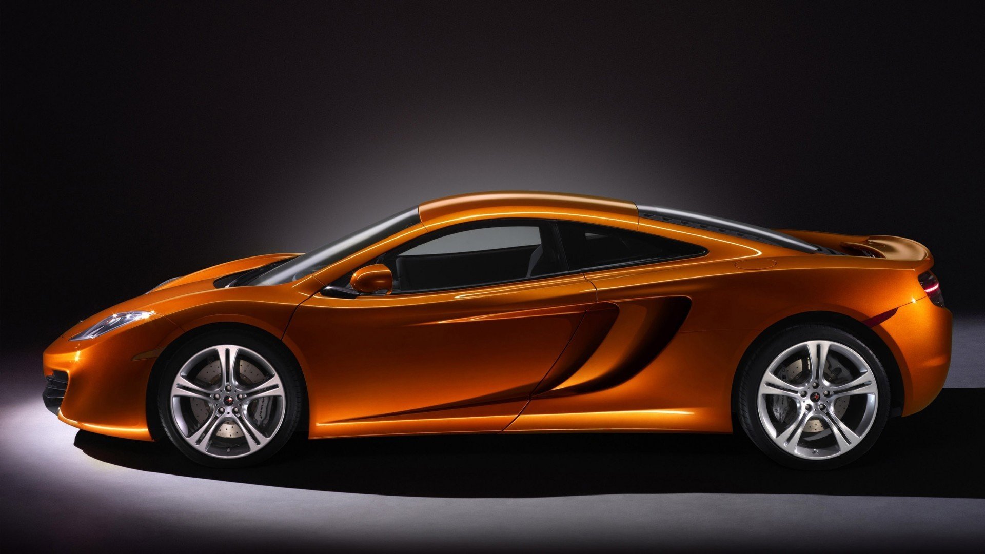 Sleek orange McLaren sports car side profile on a dark backdrop — HD PC desktop wallpaper/background featuring a high-performance vehicle.