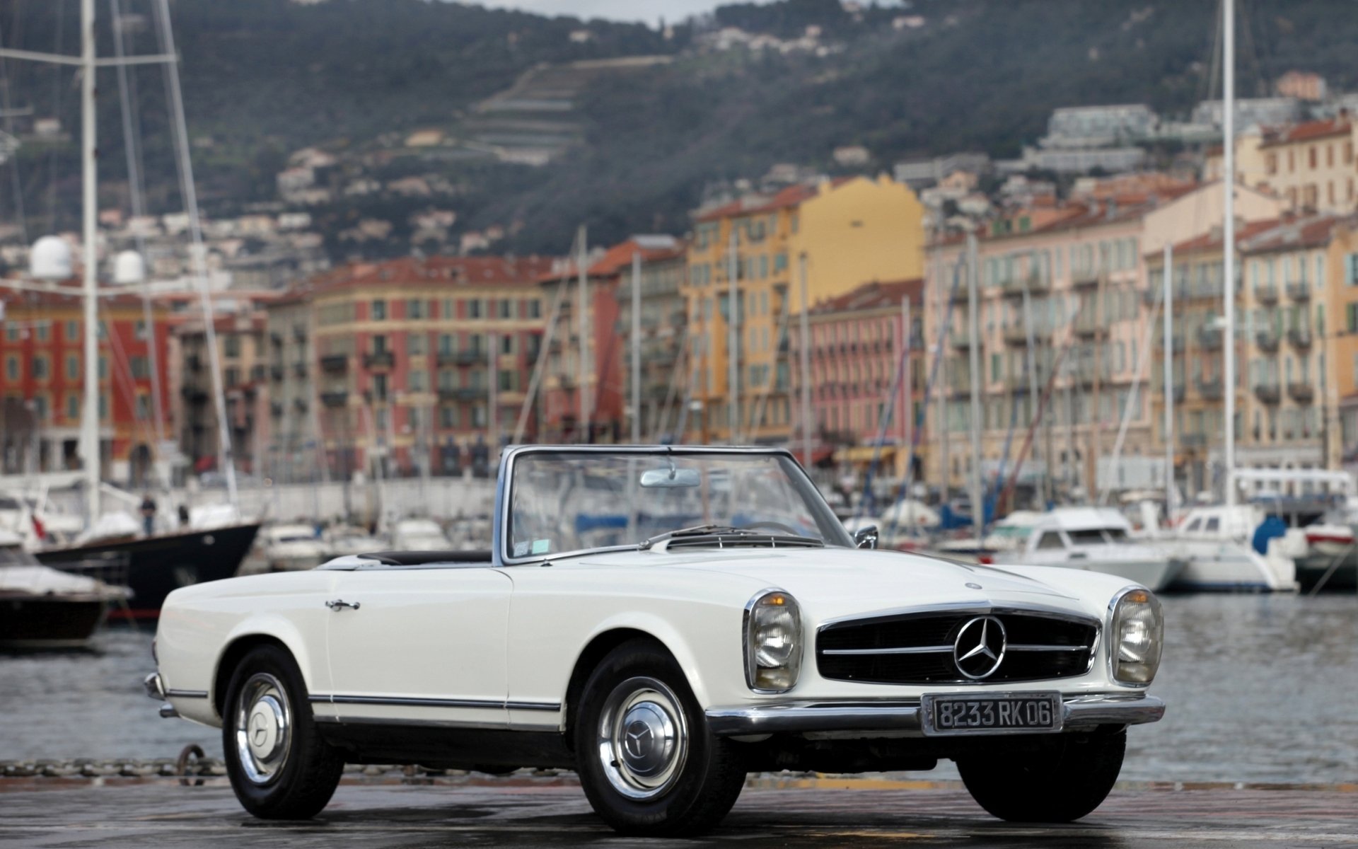 HD desktop wallpaper featuring a classic white Mercedes convertible parked by a marina with colorful buildings and hills in the background.