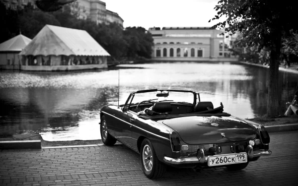 A classic MG vehicle parked by a serene lake, with a scenic background of trees and a tented structure, creating a nostalgic black-and-white wallpaper for desktop use.