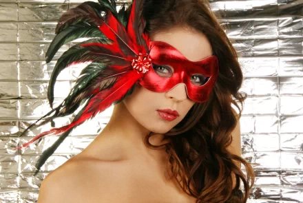 A striking HD desktop wallpaper featuring a woman in a vibrant red mask adorned with feathers, set against a shimmering silver background, showcasing dynamic photography.