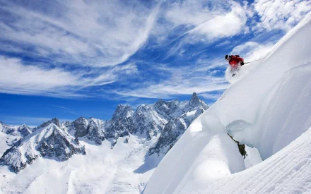 HD desktop wallpaper showing a skier descending a snowy mountain slope with rugged peaks under a vibrant blue sky, capturing the thrill of winter sports.