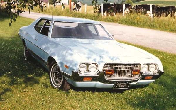 HD desktop wallpaper featuring a classic Ford Gran Torino parked on grass beside a country road with cows and greenery in the background.