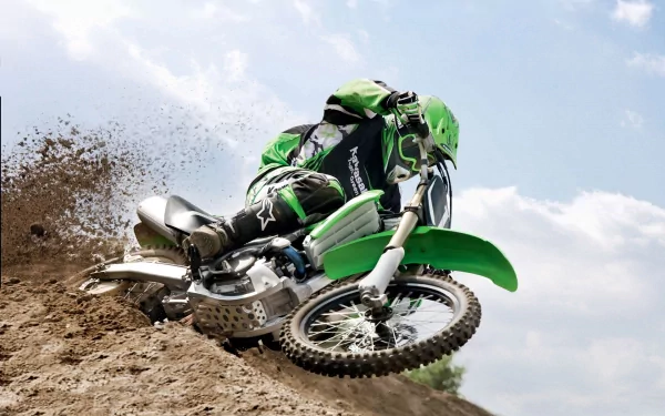 A dirt bike rider in green gear kicks up dust while navigating a turn on a motocross track. The dynamic scene captures the thrill of the sport. HD desktop wallpaper and background.