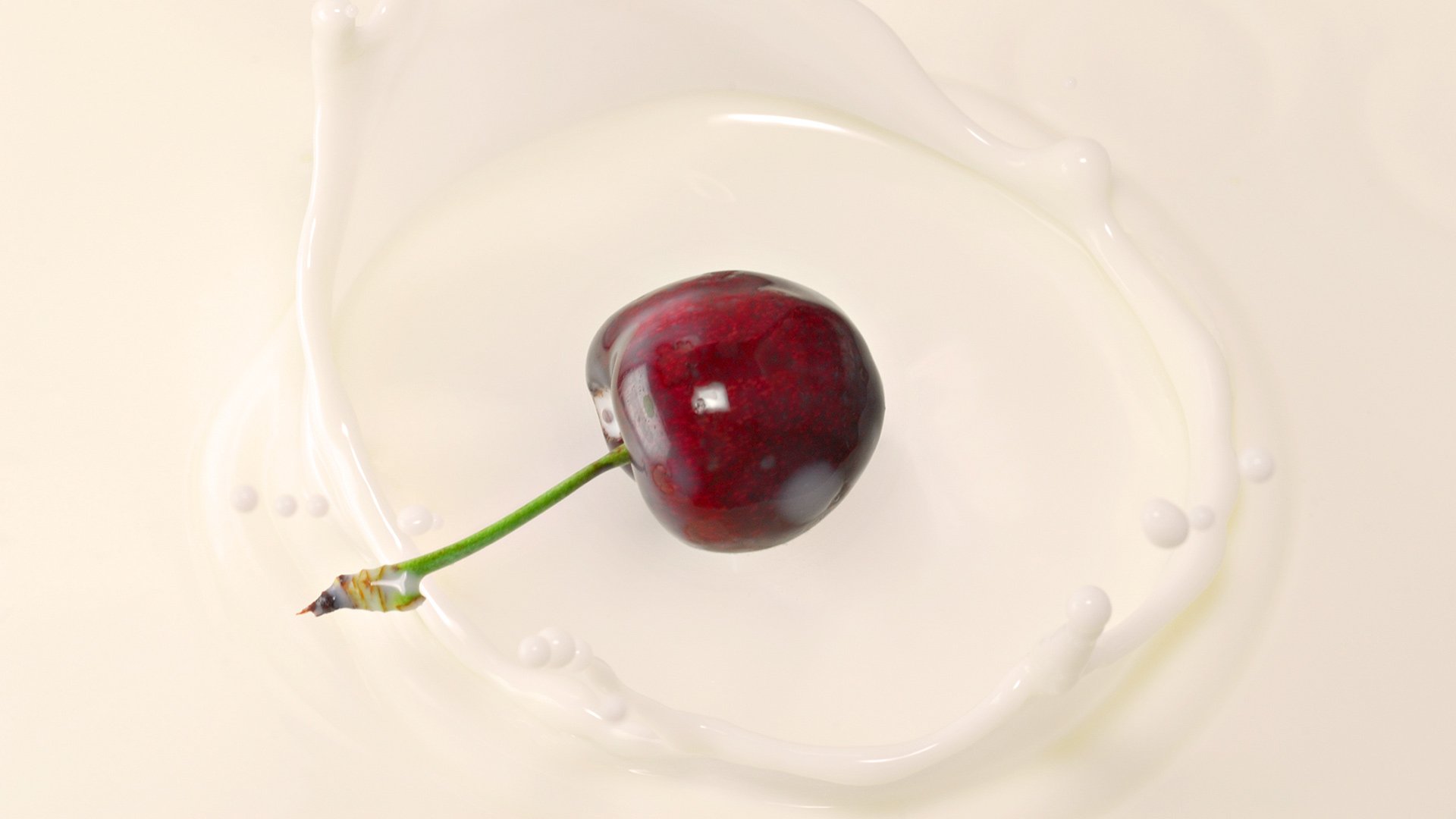 HD PC desktop wallpaper: a food-themed background showing a single ripe cherry with stem resting in a swirl of white liquid.