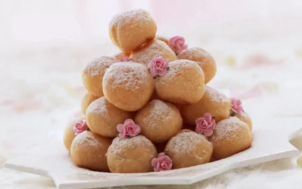 A beautifully arranged pyramid of doughnuts, dusted with powdered sugar and adorned with tiny pink roses, serves as an appetizing HD desktop wallpaper and background.