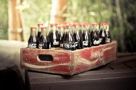 A rustic wooden crate filled with glass Coca Cola bottles, captured in 4K Ultra HD as a man-made PC desktop wallpaper background.