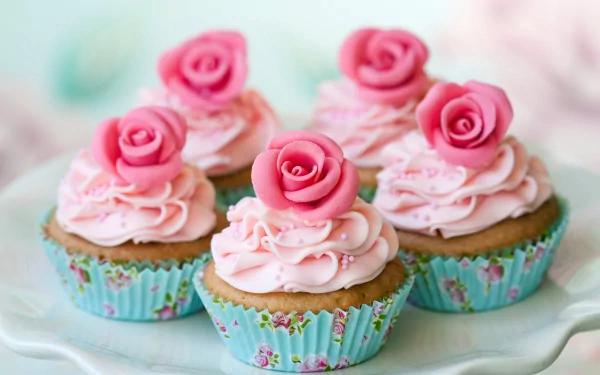 A delightful display of pink frosted cupcakes topped with rose decorations, set against a soft, pastel background. This vibrant image makes a charming 4K Ultra HD desktop wallpaper.