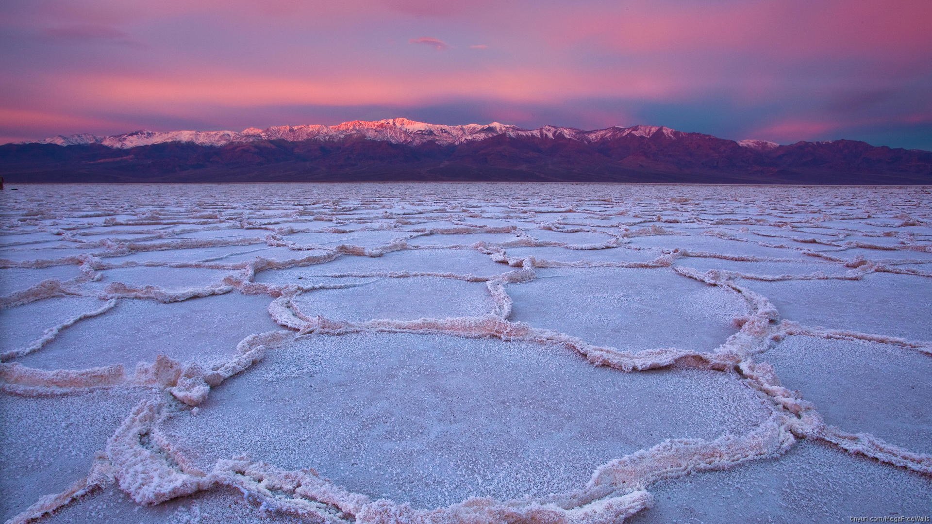 HD PC desktop wallpaper of a salt lake's polygonal salt crust in the foreground, pastel sunset sky and distant snow‑capped mountains — serene nature mountain landscape.