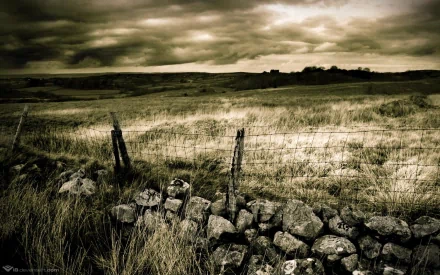 HD desktop wallpaper featuring a serene nature scene with a rocky field under a moody, cloudy sky, enclosed by a rustic fence, highlighting the tranquil beauty of the countryside.