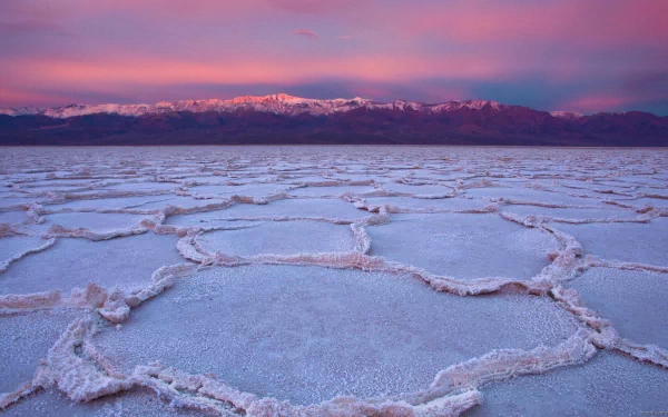 HD PC desktop wallpaper of a salt lake's polygonal salt crust in the foreground, pastel sunset sky and distant snow‑capped mountains — serene nature mountain landscape.