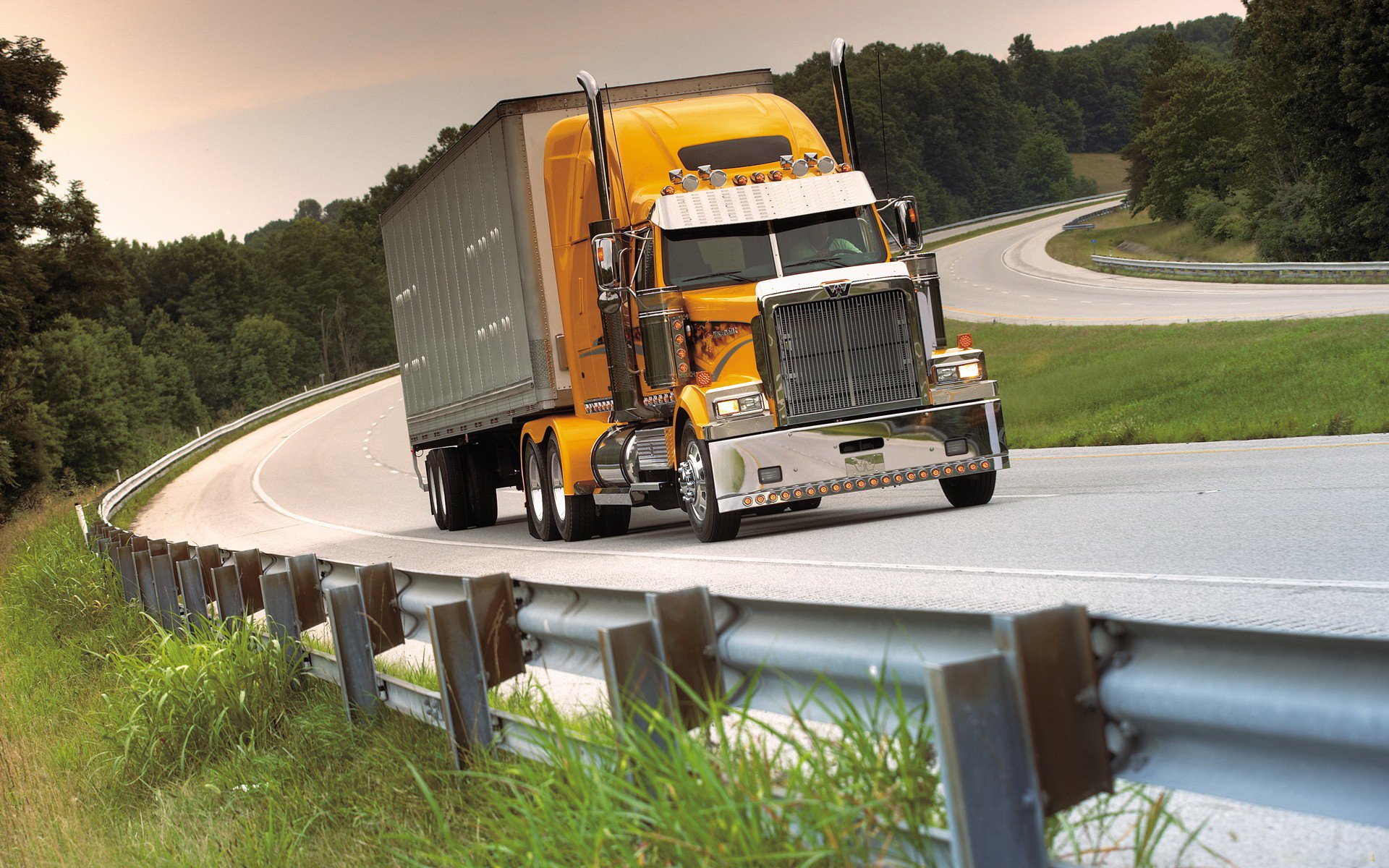 A vibrant yellow truck navigating a winding highway, set against a backdrop of greenery. This HD desktop wallpaper captures the essence of transportation and adventure.
