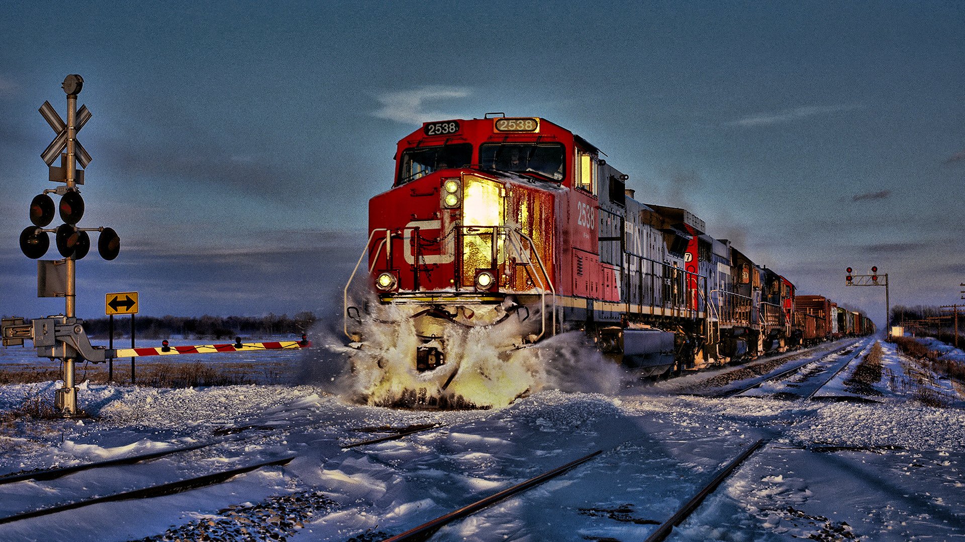 HD desktop wallpaper showing a powerful red train moving along snowy tracks at dusk, highlighting the vehicle's strength and motion.