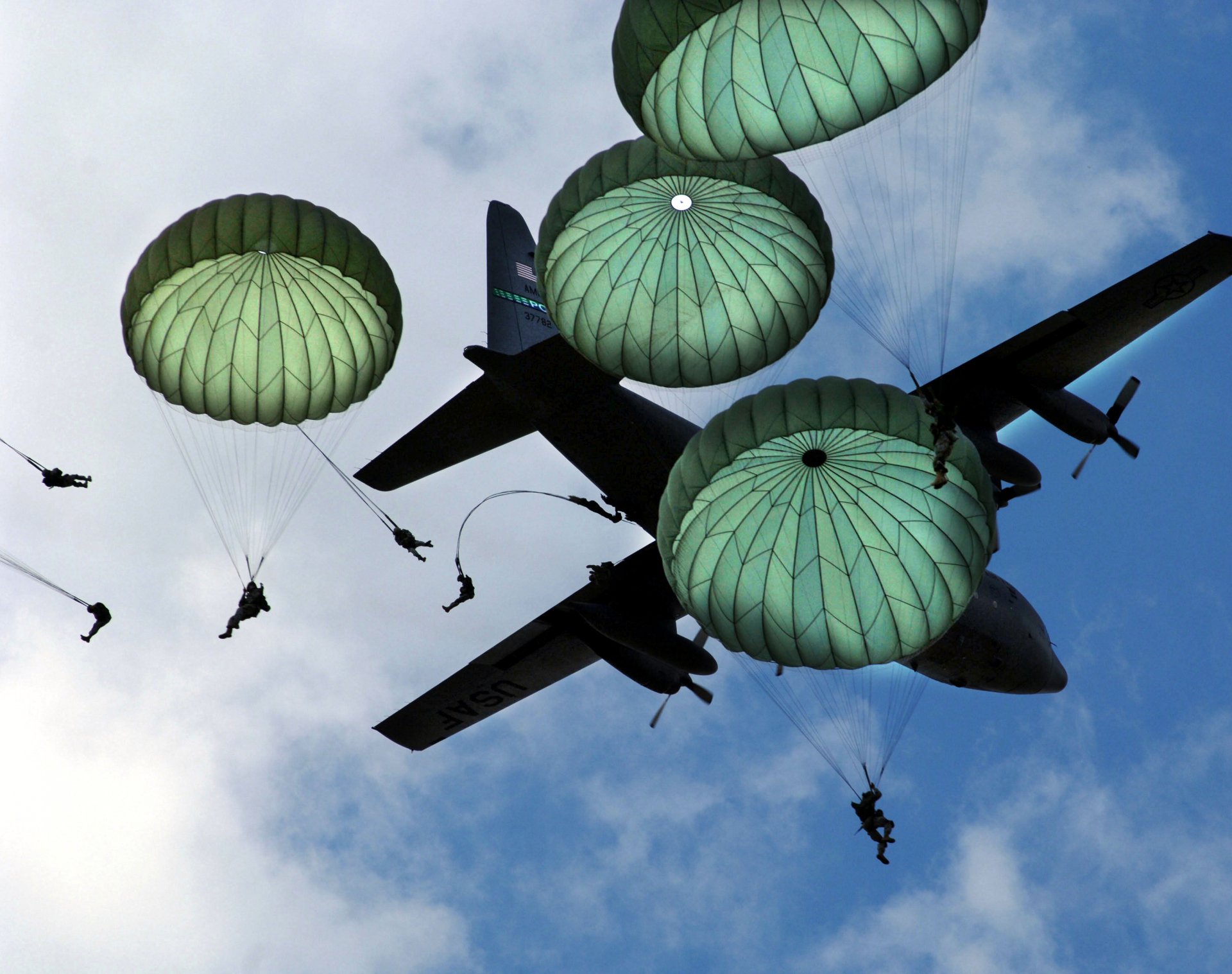 HD desktop wallpaper showing military paratroopers descending from a cargo plane against a partly cloudy sky.
