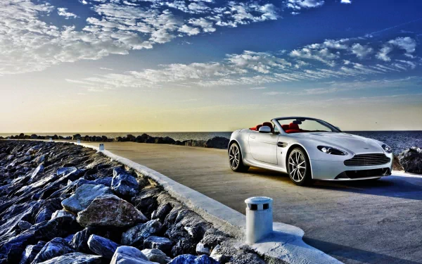 Silver Aston Martin V8 Vantage convertible driving on a coastal road under a vibrant blue sky, captured as an HD PC desktop wallpaper and background.