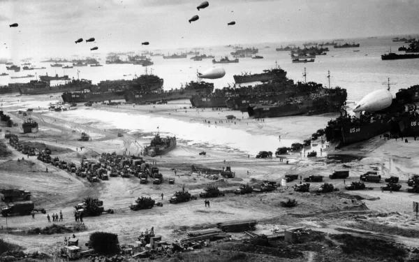 Black and white World War II battle scene with military ships, vehicles, and blimps along a crowded beach, captured in high-definition for a PC desktop wallpaper.