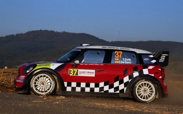HD PC desktop wallpaper: red Mini Countryman WRC rallying vehicle (No. 37) with checkerboard livery, poised on a dirt road against rolling hills — WRC racing background.