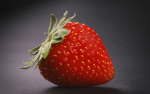HD wallpaper featuring a vivid, fresh strawberry with a green stem, set against a plain, dark background.